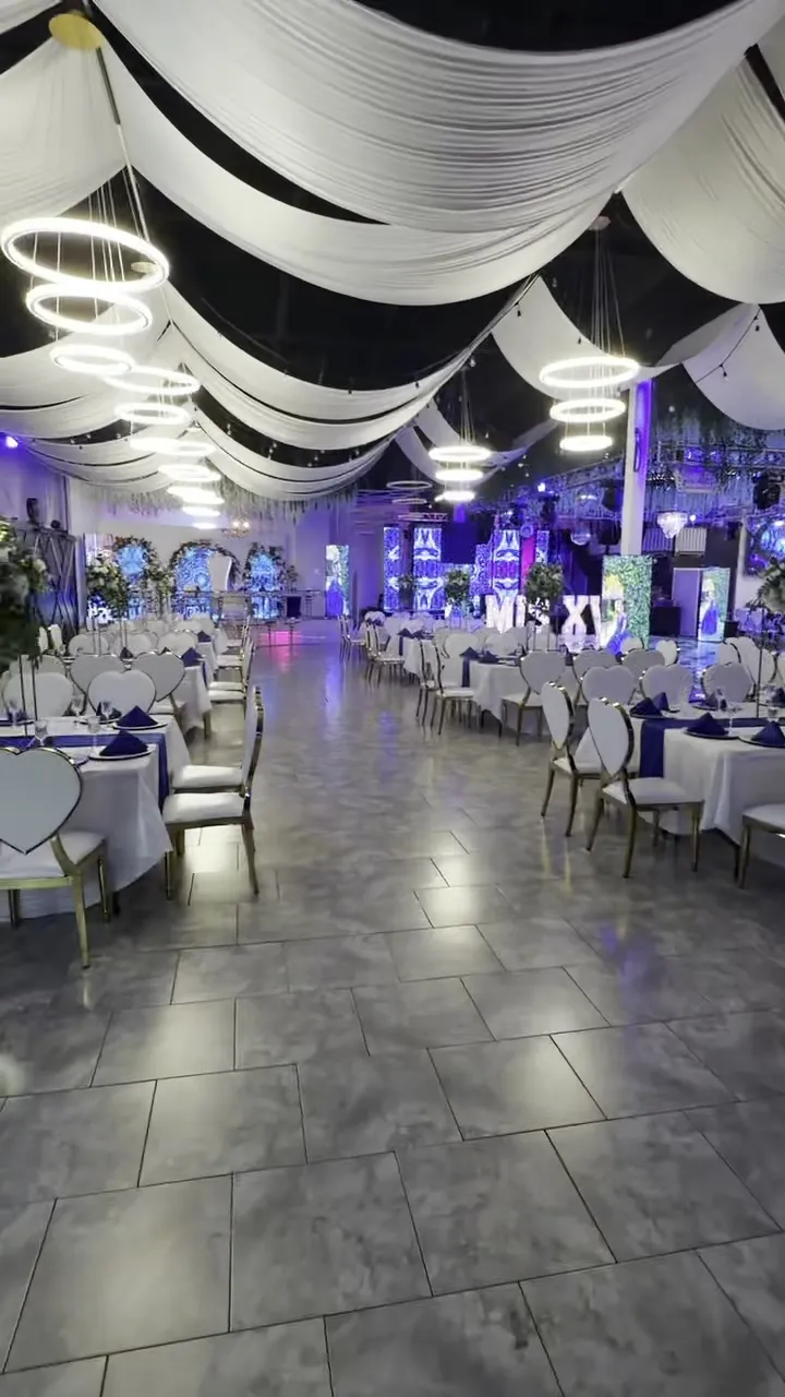 El salón principal con mesas redondas bajo un techo decorado con telas blancas y candelabros circulares.