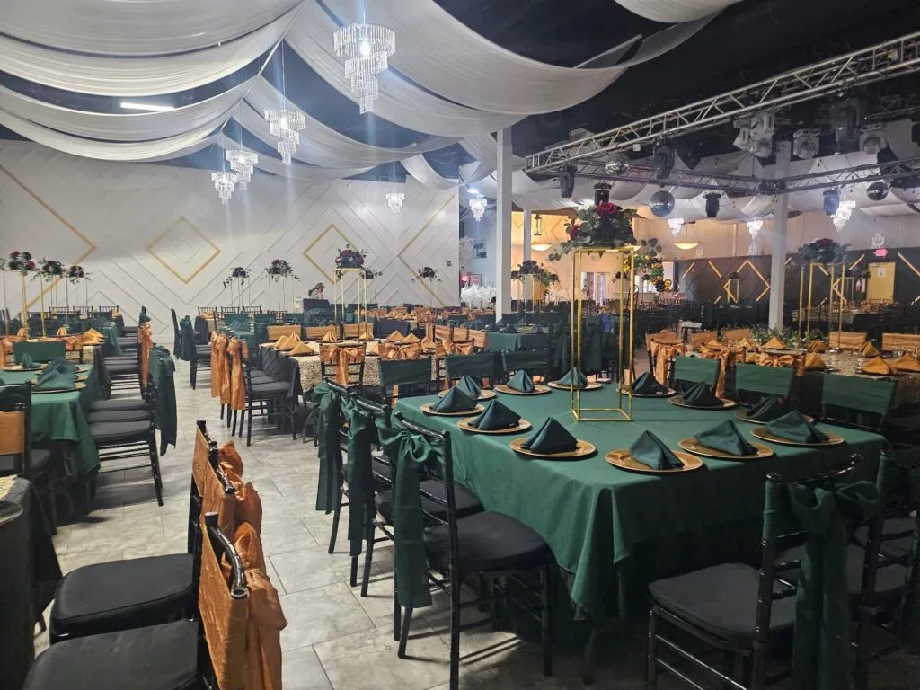 Mesas largas de banquete vestidas en verde esmeralda con moños dorados en las sillas.